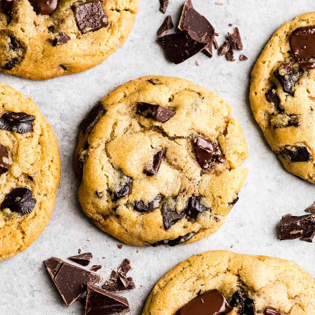 Αυτή είναι η καλύτερη συνταγή για chocolate chip cookies που έχετε δοκιμάσει ποτέ. Χωρίς περίεργα υλικά, χωρίς χρόνο ψύξης, κ.λπ. Απλά ένα απλό, εύκολο στην παρασκευή του, απίστευτα νόστιμο, ζυμαρένιο αλλά πλήρως ψημένο, cookie με κομματάκια σοκολάτας που βγαίνει τέλειο κάθε φορά! #cookies #chocolatechipcookies #baking #recipe #chocolate Προβολή από πάνω ενός chocolate chip cookie περιτριγυρισμένου από άλλα τέσσερα chocolate chip cookies και ψιλοκομμένη σοκολάτα