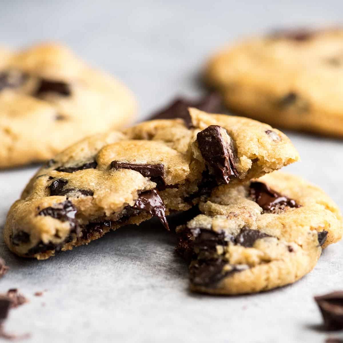 Αυτή είναι η καλύτερη συνταγή για chocolate chip cookies που έχετε δοκιμάσει ποτέ. Χωρίς περίεργα υλικά, χωρίς χρόνο ψύξης, κ.λπ. Απλά ένα απλό, εύκολο στην παρασκευή του, απίστευτα νόστιμο, ζυμαρένιο αλλά πλήρως ψημένο, cookie με κομματάκια σοκολάτας που βγαίνει τέλειο κάθε φορά! #cookies #chocolatechipcookies #baking #recipe #chocolate Μπροστινή όψη ενός chocolate chip cookie κομμένου στη μέση με λιωμένα κομματάκια σοκολάτας