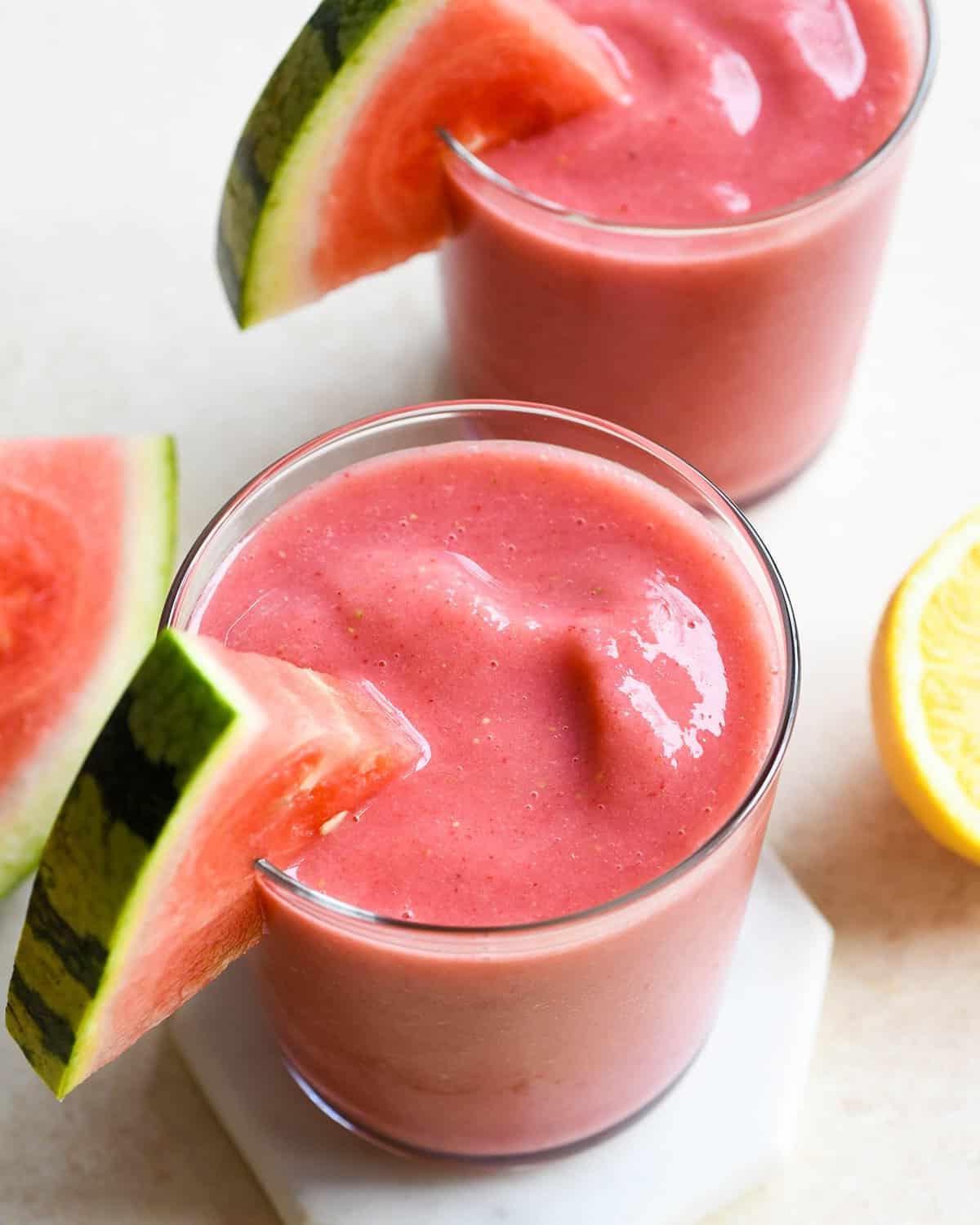 Δύο ποτήρια γεμάτα smoothie καρπούζι με φέτες καρπουζιού στα χείλη