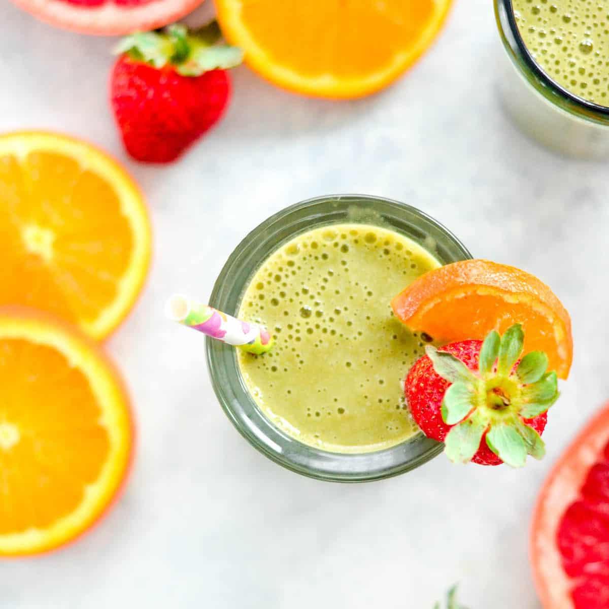 Πάνω όψη ενός πράσινου smoothie εσπεριδοειδών με καλαμάκι και γαρνιτούρα από φέτα πορτοκαλιού και φράουλα