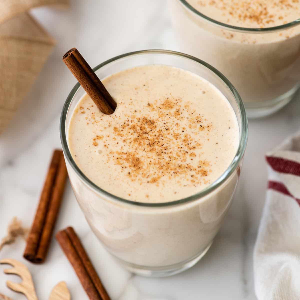 Συνταγή για Σπιτικό Εγκνογκ 3 Δύο ποτήρια Eggnog με ένα ξυλάκι κανέλας και τριμμένο μοσχοκάρυδο στην κορυφή