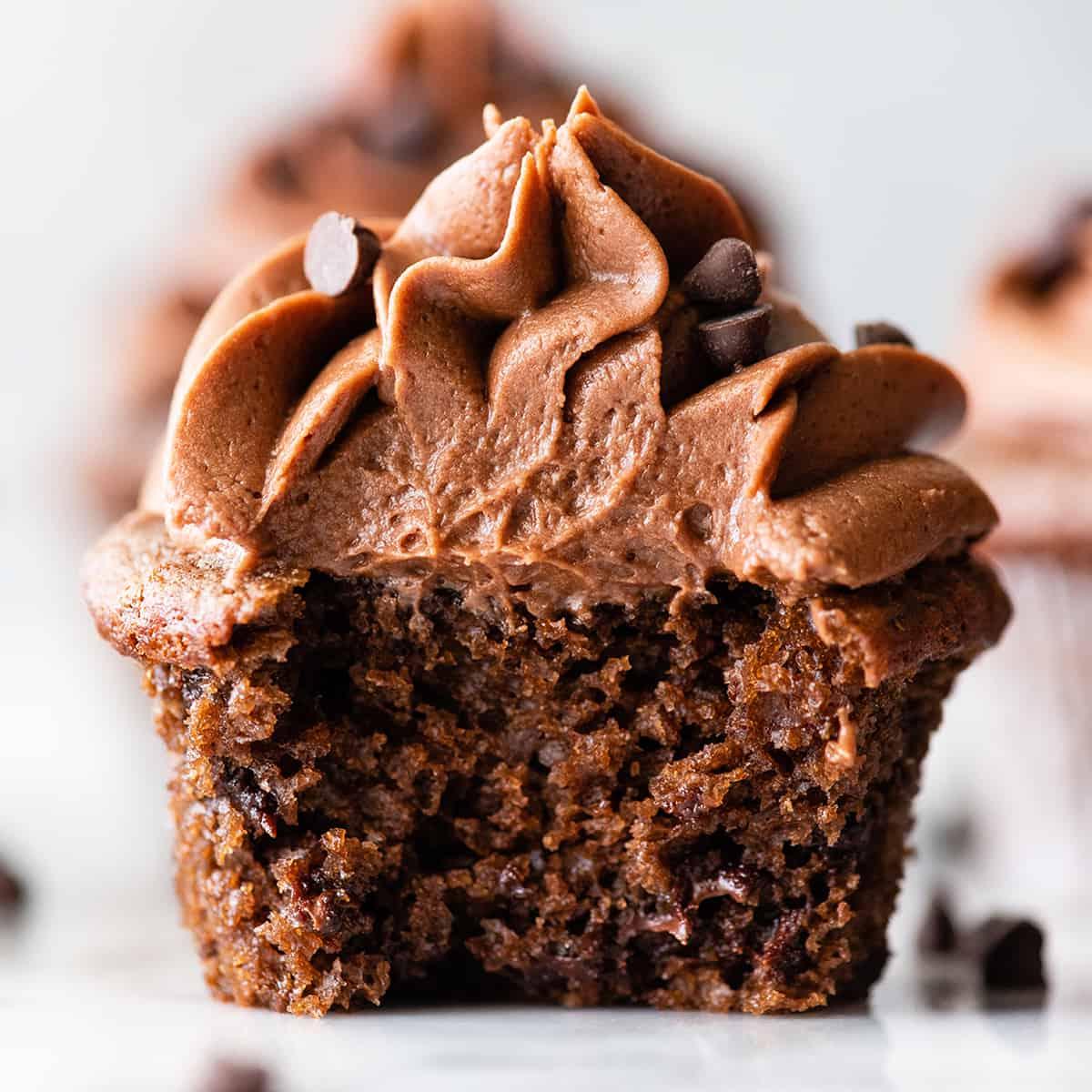 Αυτή η συνταγή για σοκολατένια cupcakes είναι εύκολη στην παρασκευή από το μηδέν με απλά υλικά. Είναι τα καλύτερα, ζουμερά σοκολατένια cupcakes με πλούσια γεύση σοκολάτας και τέλεια υφή. Κοντινή μπροστινή όψη ενός σοκολατένιου cupcake κομμένου στη μέση με γλάσο σοκολάτας