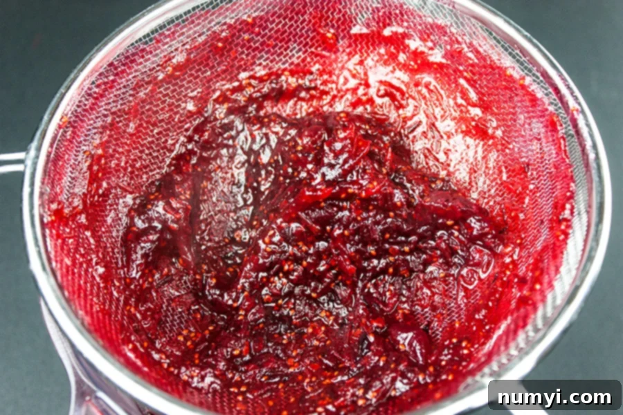 Easy Homemade Cranberry Sauce Your Way 4 Cranberry sauce being pushed through a strainer.