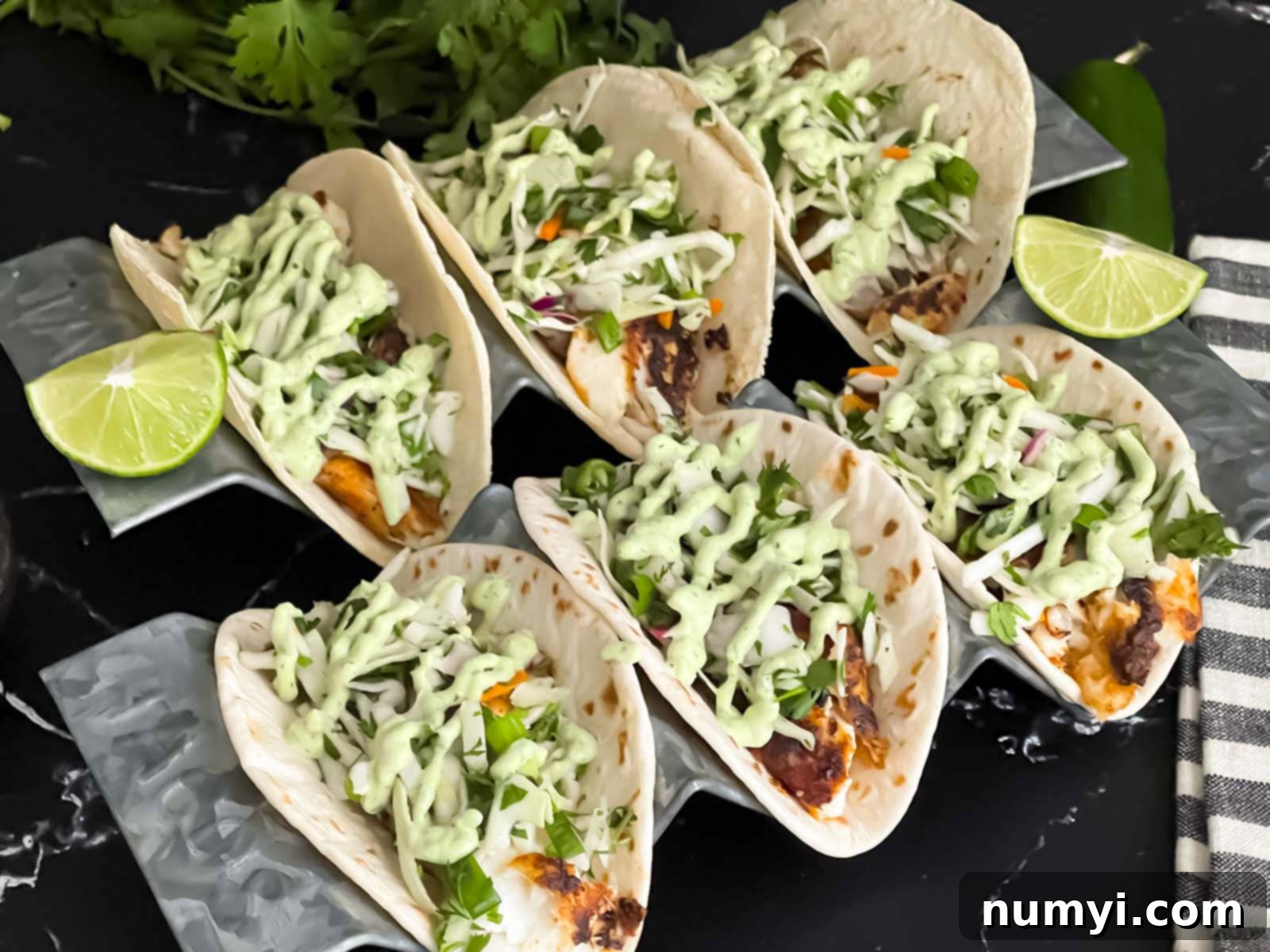 Blackened Fish Tacos on a dark background, garnished with fresh cilantro and lime wedges.
