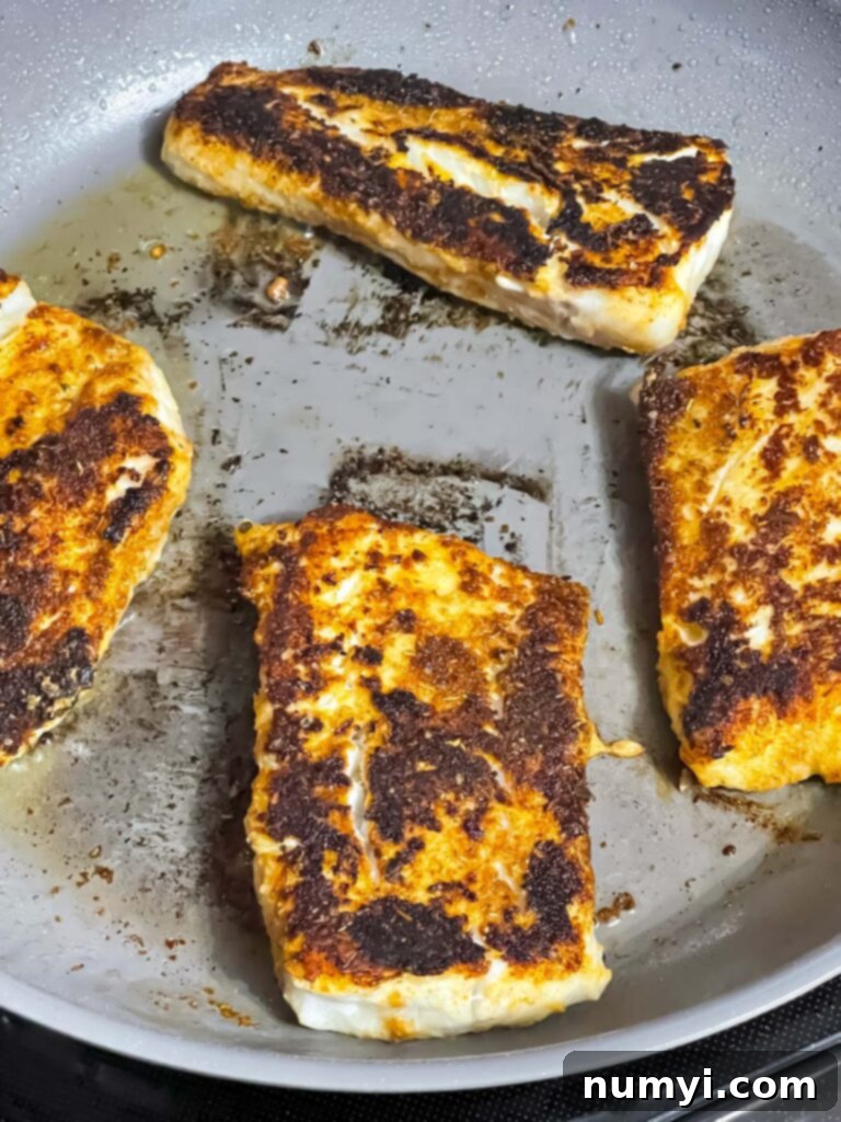 Perfectly blackened fish, showing a dark, crispy crust, in a skillet.