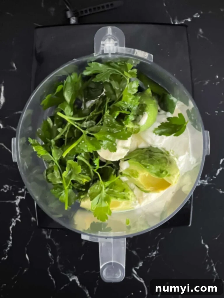 All the ingredients for the avocado sauce, including cilantro, avocado, and jalapeno, in a food processor.