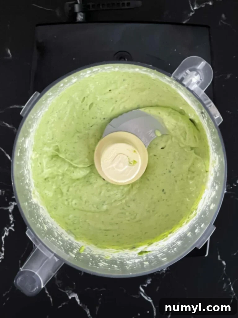 Smooth, vibrant green avocado sauce blended in a food processor, ready for the tacos.