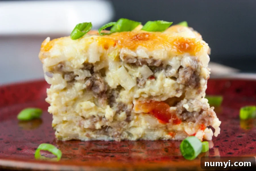 A vibrant slice of sausage hashbrown breakfast casserole, perfectly golden, served on a cheerful red plate and garnished with fresh green onions.