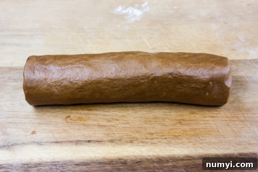 Crispy Gingersnap Cookies dough rolled into a log on a wooden cutting board, ready for chilling.