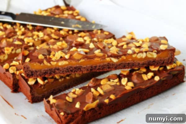 layered Peanut Butter and Caramel Brownies cut into slices with nut topping, showcasing the distinct chocolate, caramel, and peanut butter layers