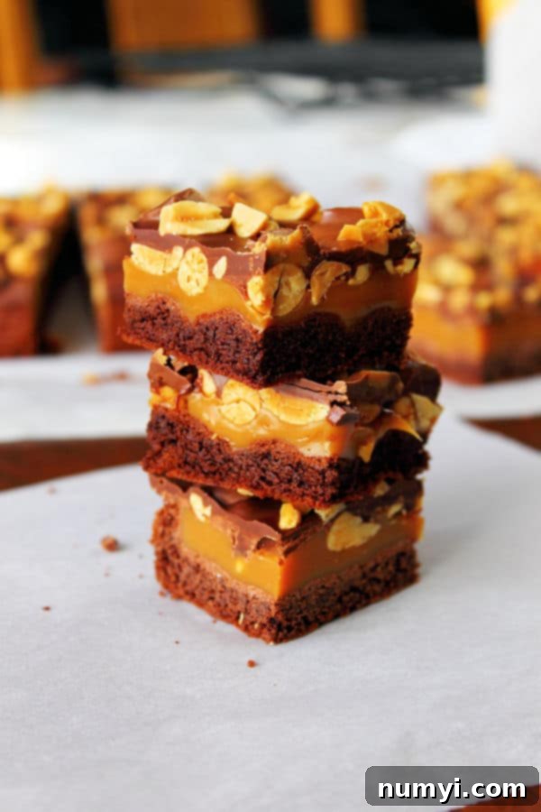 three peanut butter caramel brownies cut into squares and stacked on top of each other, showing the thick layers