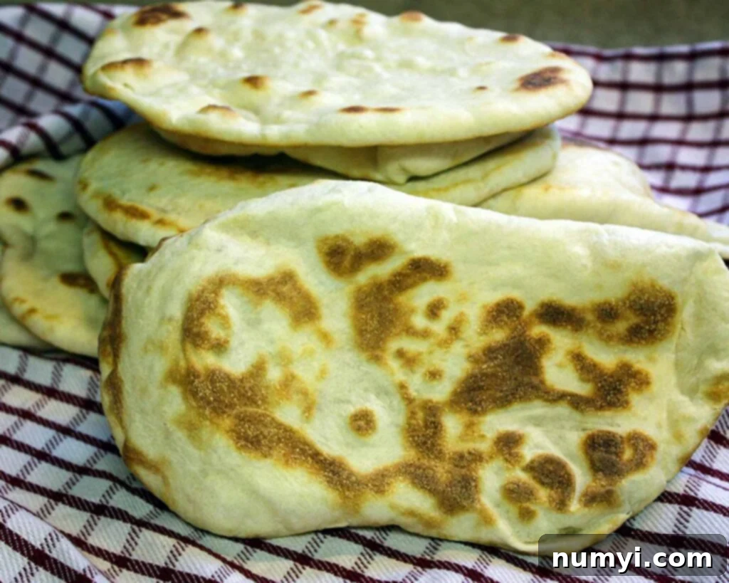 Homemade naan flatbread stacked on a red and white kitchen towel.