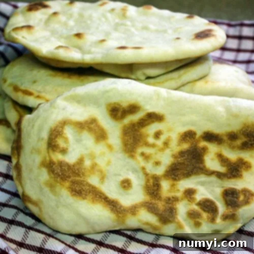 Homemade naan flatbread stacked on a red and white kitchen towel.