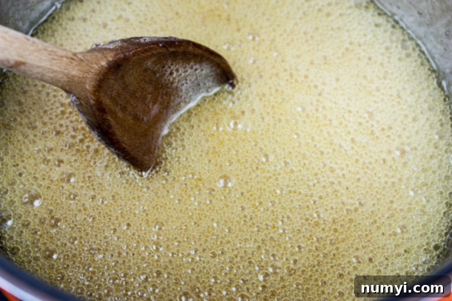 Classic Homemade Peanut Brittle 4 Close-up of sugar, water, and corn syrup simmering vigorously in a large saucepan on the stovetop, just beginning its caramelization journey.