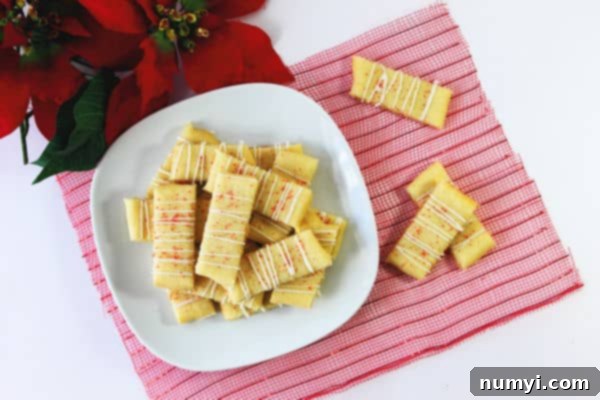 Swedish butter cookies on a white plate and red fabric with icing and red sprinkles on them beside a poinsettia