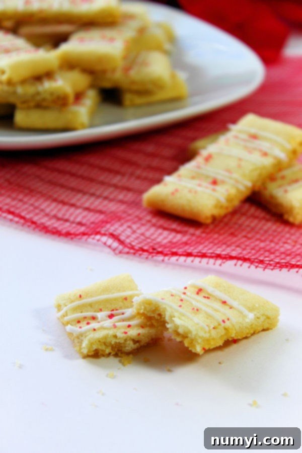 Swedish Butter Cookies on a white plate and out of focus in the background with a couple in the midground on a red fabric, and one cookie broken in half in the foreground on a white surface