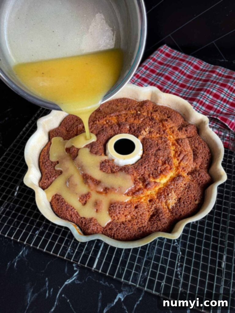 Spiced Eggnog Bundt with Creamy Glaze 6 Warm eggnog glaze being poured generously over the still-warm Eggnog Bundt Cake in its pan, allowing it to soak into the poked holes.