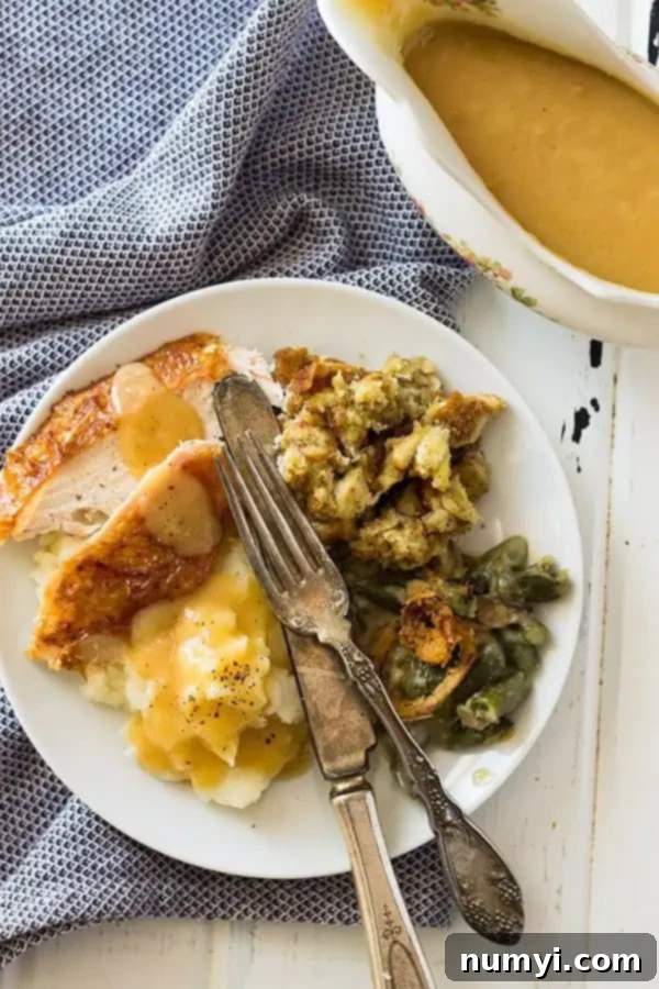 Overhead shot of herb roasted turkey on a plate, surrounded by Thanksgiving sides like stuffing, mashed potatoes, and gravy.