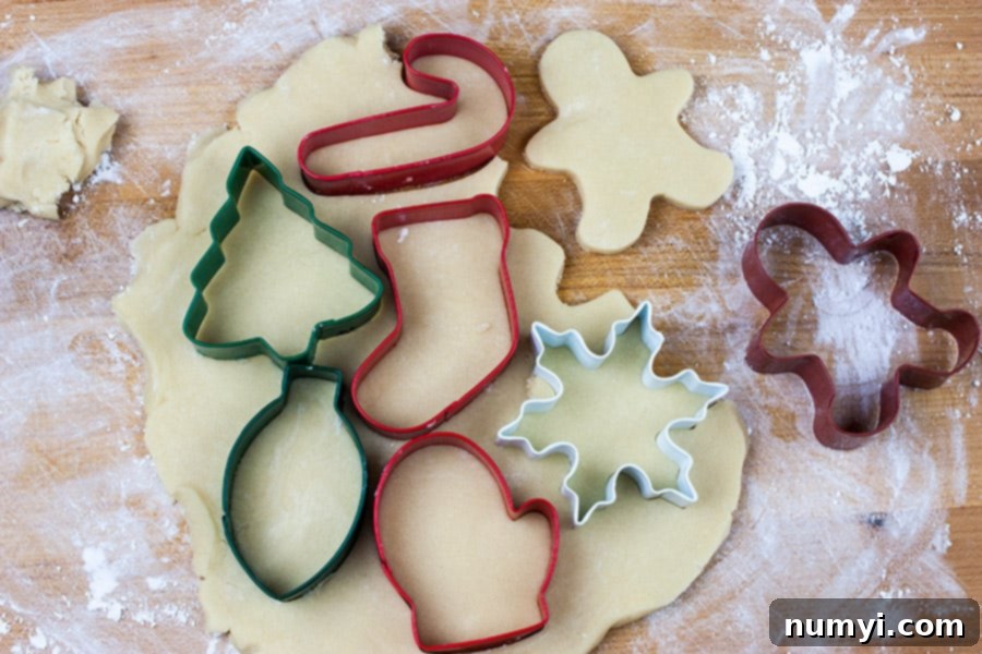 Sugar cookie dough rolled out with various cookie cutters pressed into it on a countertop.