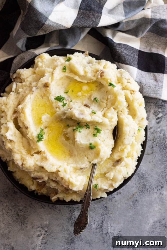 Large bowl of slow cooker mashed potatoes with pools of melted butter and chopped parsley for garnish.