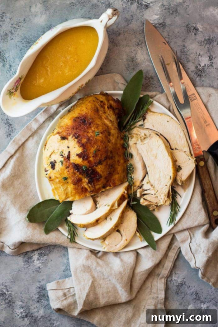 Top down view of a perfectly cooked slow cooker turkey breast on a white serving platter, accompanied by a small bowl of rich, brown gravy.