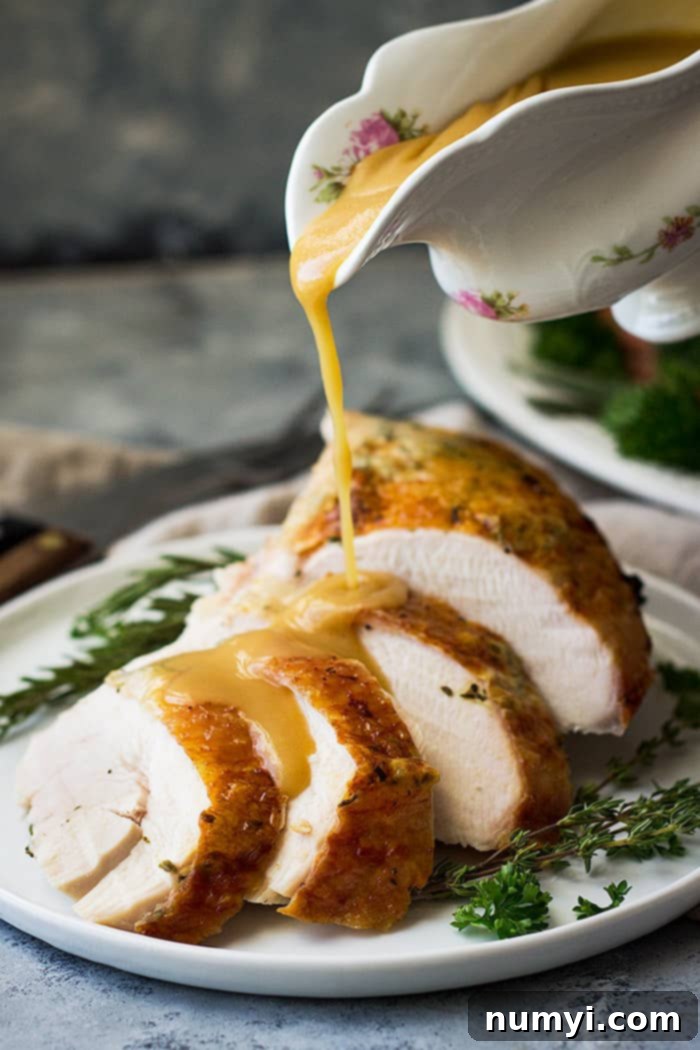 Close-up of a serving of sliced slow cooker turkey breast on a white plate, with gravy being poured over it and garnished with fresh herbs.