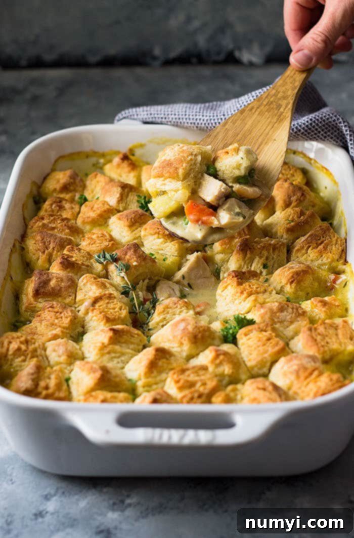 Homestyle Chicken & Biscuit Pot Pie 2 Wooden spoon scooping out creamy chicken pot pie from white baking dish with golden biscuit topping.