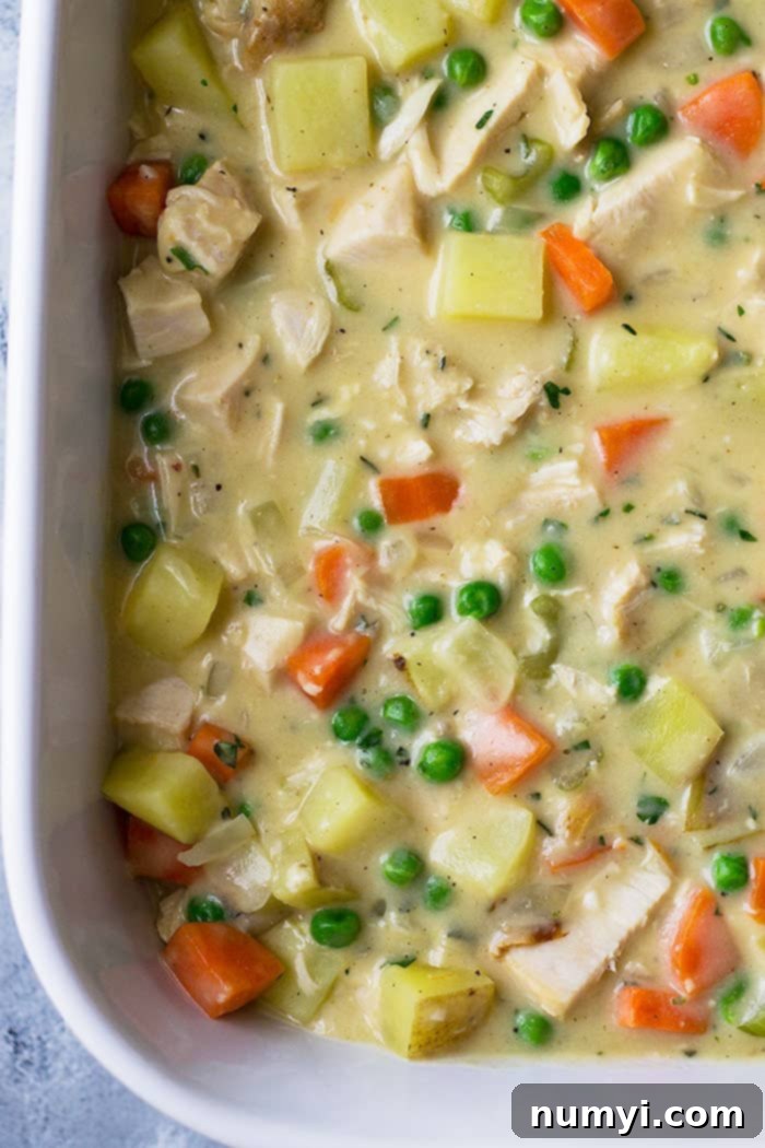 Homestyle Chicken & Biscuit Pot Pie 4 Creamy chicken pot pie filling with mixed vegetables in a white baking dish before biscuit topping is added.