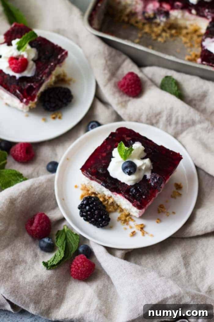 overhead: a slice of raspberry pretzel salad on a white plate with mixed berries and whipped cream on top