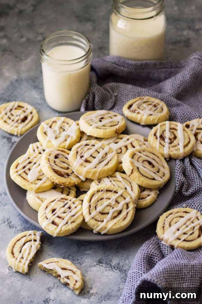 Cinnamon roll cookies piled on a plate with jars of milk in the background, showcasing their delicious swirl and inviting texture.