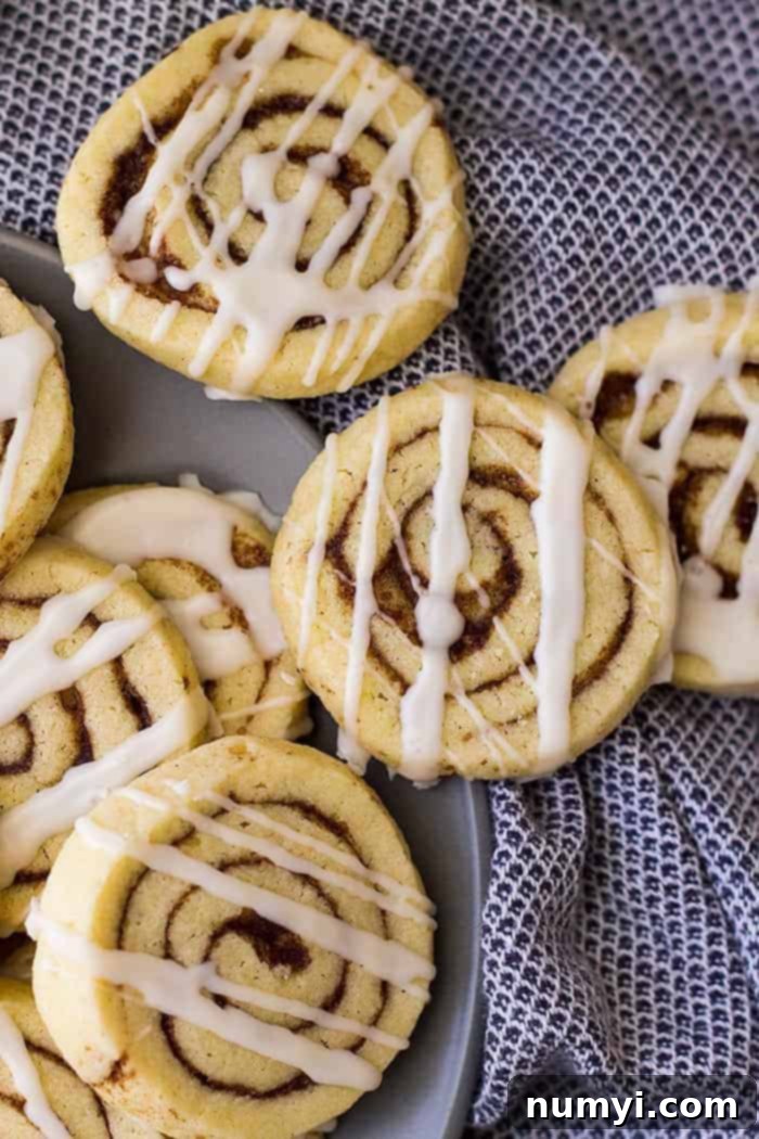 Close up shot of cinnamon roll spiral cookies drizzled with icing, highlighting the beautiful swirl pattern and glistening glaze.
