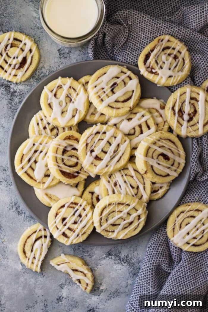 Cinnamon roll sugar cookies drizzled with icing, artfully piled on and around a gray plate, ready to be enjoyed.