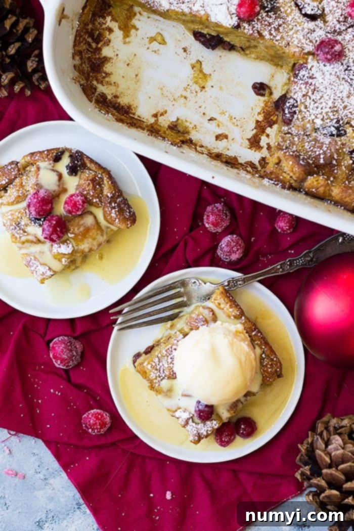 Overhead shot of cranberry bread pudding in a large baking dish, adorned with scoops of melting vanilla ice cream and scattered sugared cranberries, creating an inviting holiday visual.
