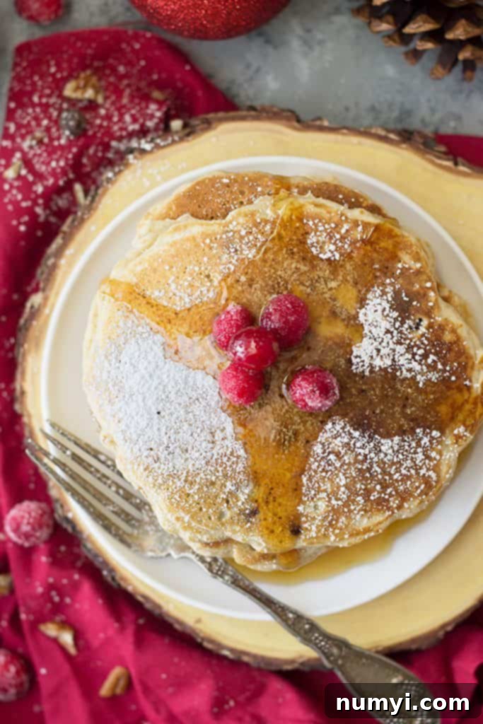 Top down view of cranberry chocolate chip pancakes drizzled with syrup and dusted with powdered sugar.
