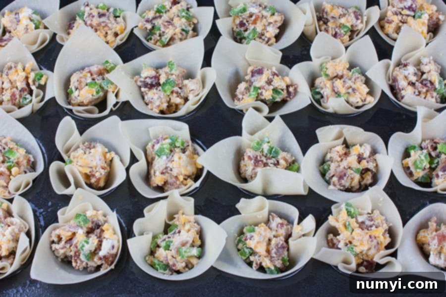 Mini muffin pan filled with wonton wrappers, each containing a spoonful of savory jalapeno popper filling before baking.