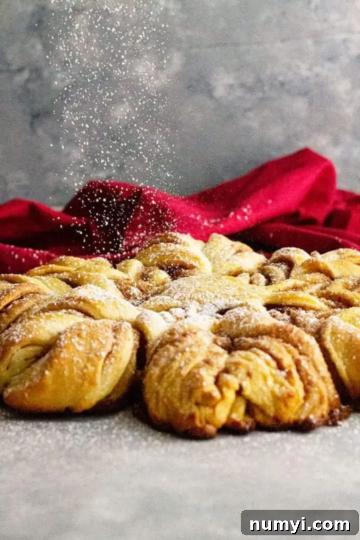 A close-up of the cinnamon snowflake bread being sprinkled with powdered sugar, adding a festive, finished touch.