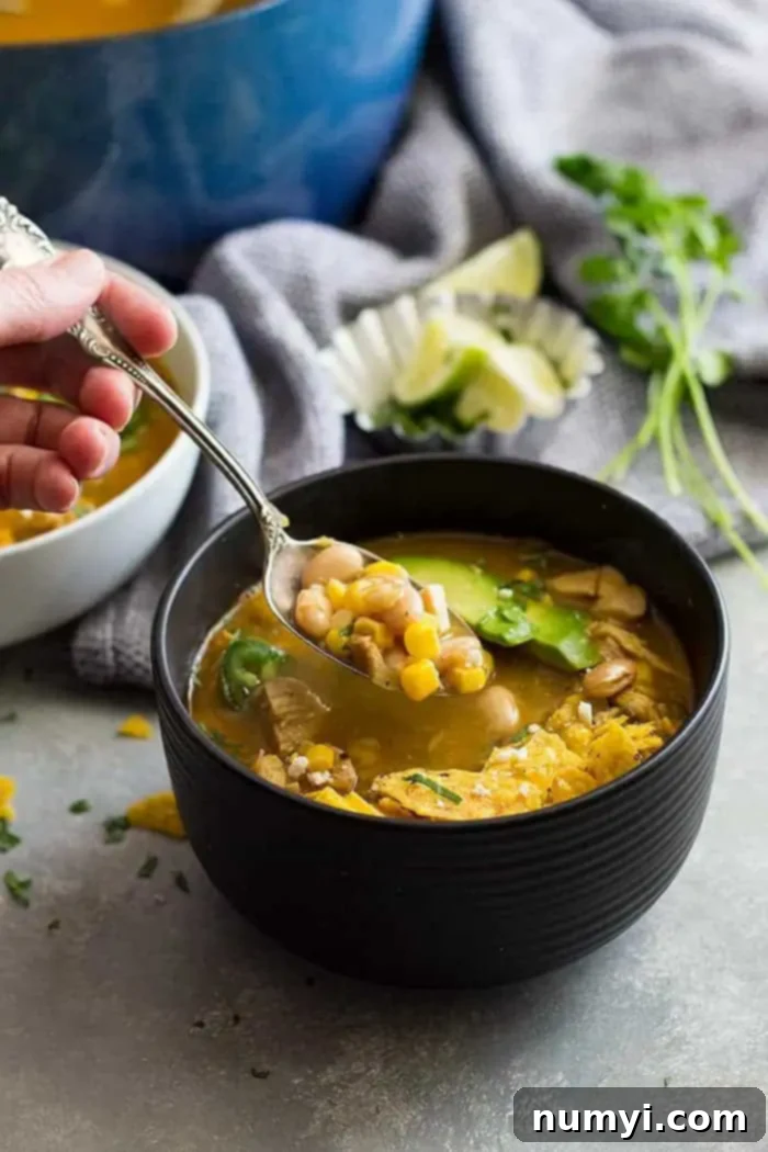 a hand holding a spoon of easy white chicken chili over a bowl of soup