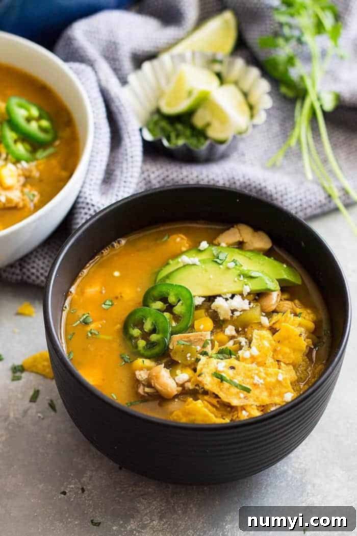 a bowl white chicken chili with rotisserie chicken with tortilla, chiles, and avocado on top