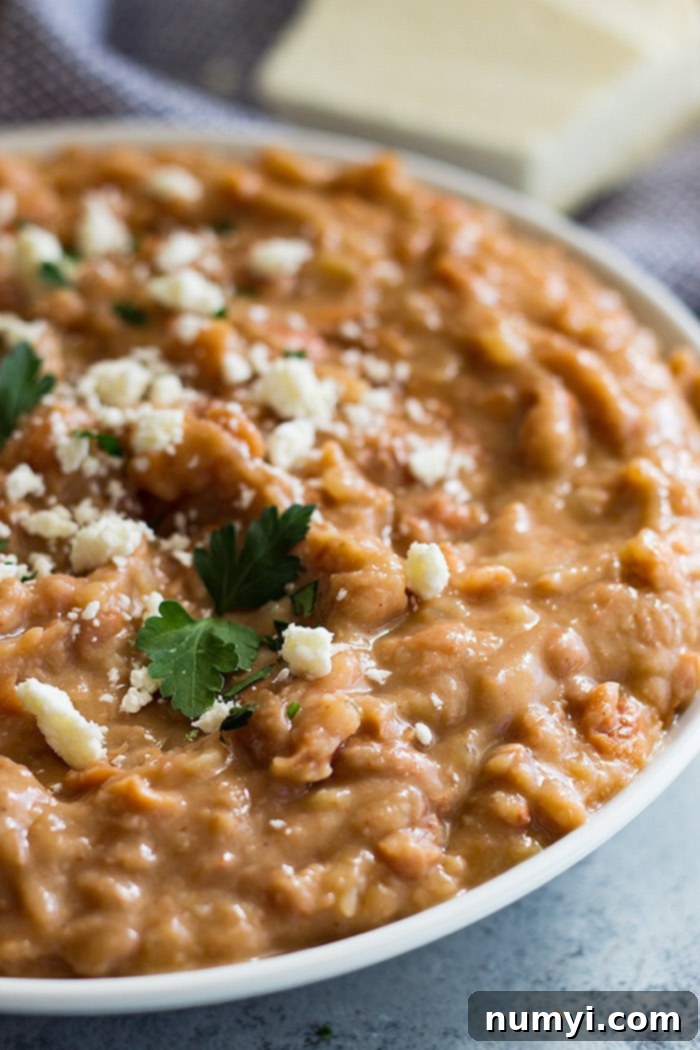 A large bowl of creamy, homemade refried beans topped with a generous sprinkle of shredded cheese.