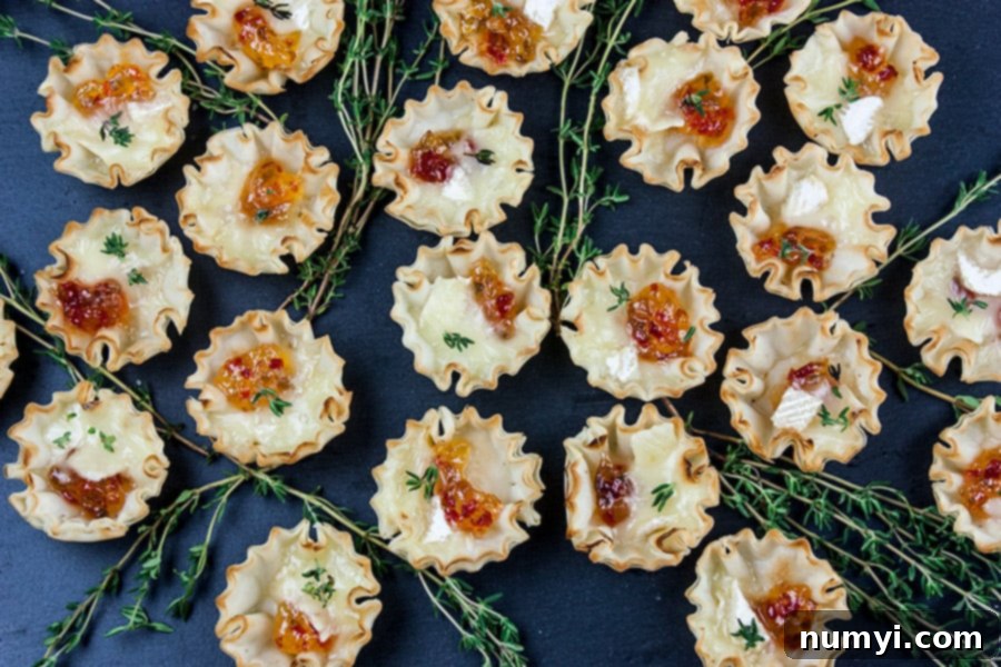 Pepper Jelly Brie Bites, perfectly baked with melted brie and jelly, arranged on a black slate serving board and garnished with fresh thyme sprigs.