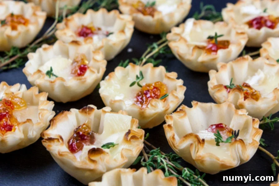 Close up view of perfectly baked Pepper Jelly Brie Bites on a black slate, adorned with small sprigs of fresh thyme, highlighting the melted cheese and vibrant jelly.