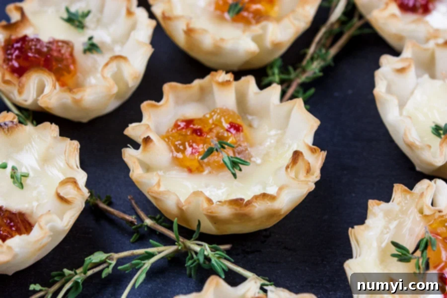 Close up of pepper jelly brie bite on slate with fresh thyme sprig garnish.