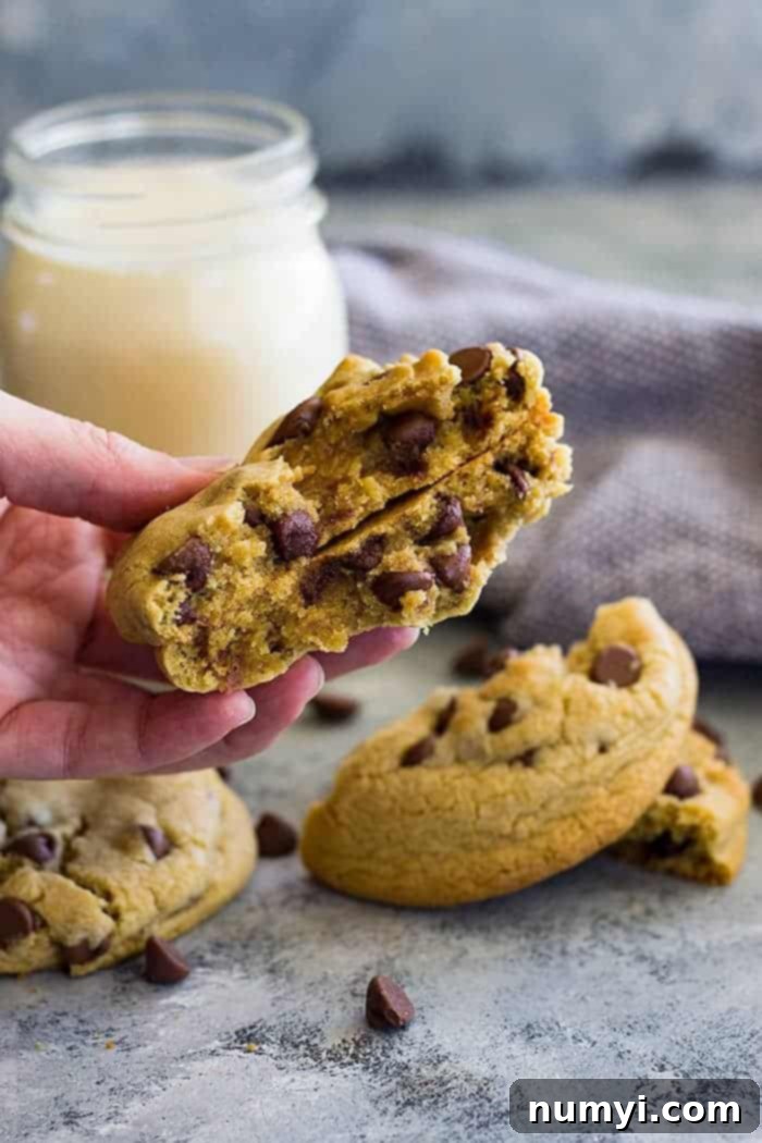 Just Enough Chocolate Chip Cookies 4 A hand holding two halves of a cookie for two showing the center. Milk and cookies in the background.
