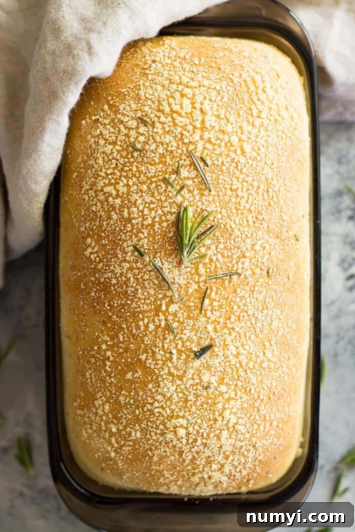 Top down view of a golden brown loaf of Rosemary Parmesan Bread, garnished with fresh rosemary sprigs.