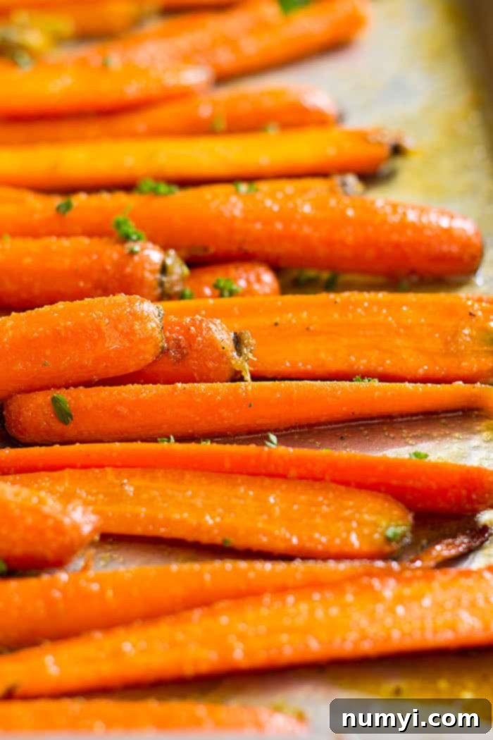 Close up view of perfectly roasted honey garlic carrots, glistening with glaze on a baking sheet.
