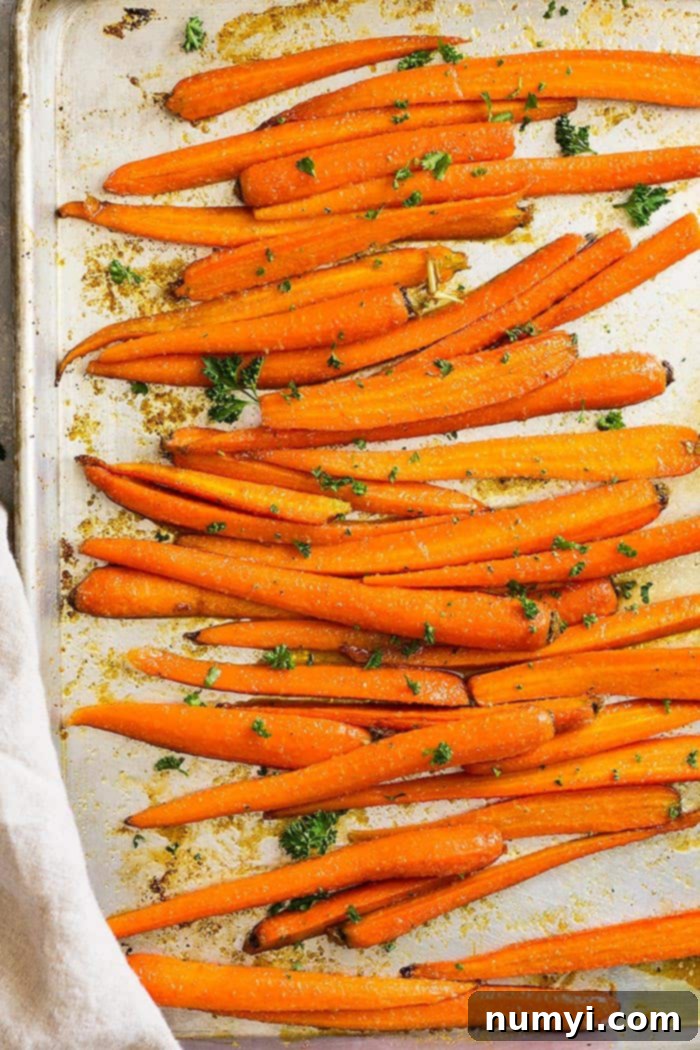 Top down view of honey garlic roasted carrots on a sheet pan, garnished with fresh herbs.