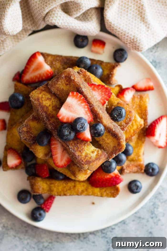 overhead shot of fried french toast sticks on a white plate with fresh berries scattered. 