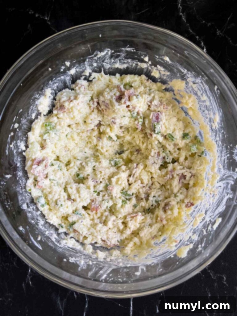 The unbaked loaded cauliflower mash casserole mixture in a glass bowl, showing its creamy consistency.