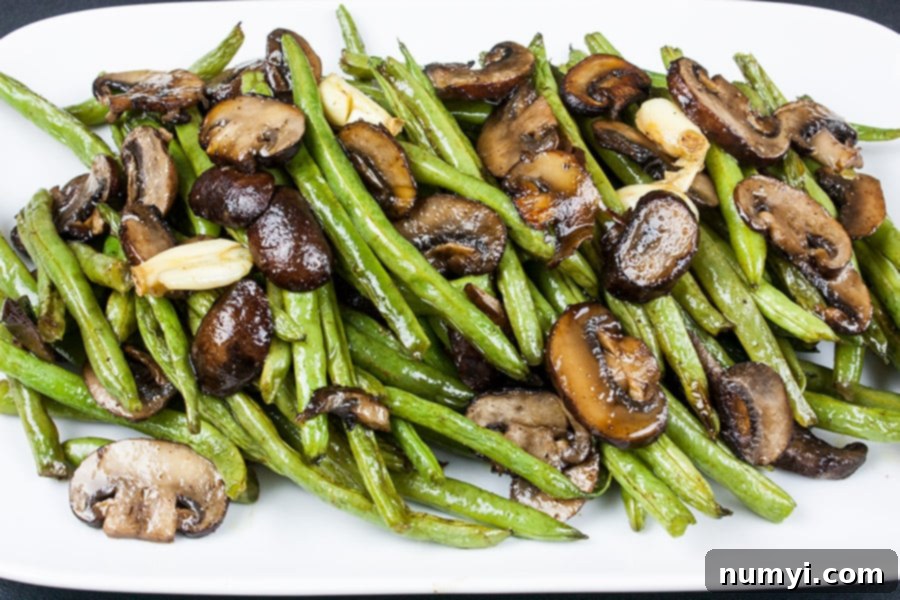 A serving platter showcasing perfectly roasted green beans and crimini mushrooms, glistening with garlic-infused oil.