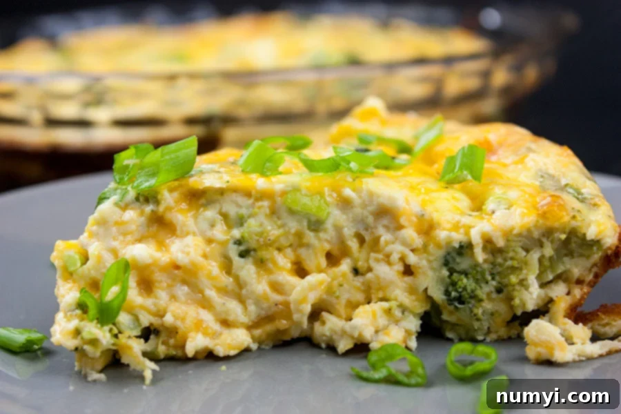 A perfectly sliced piece of golden-brown crustless broccoli cheddar quiche, garnished with fresh diced green onions, resting on a stylish gray plate. The creamy texture and vibrant broccoli are clearly visible.
